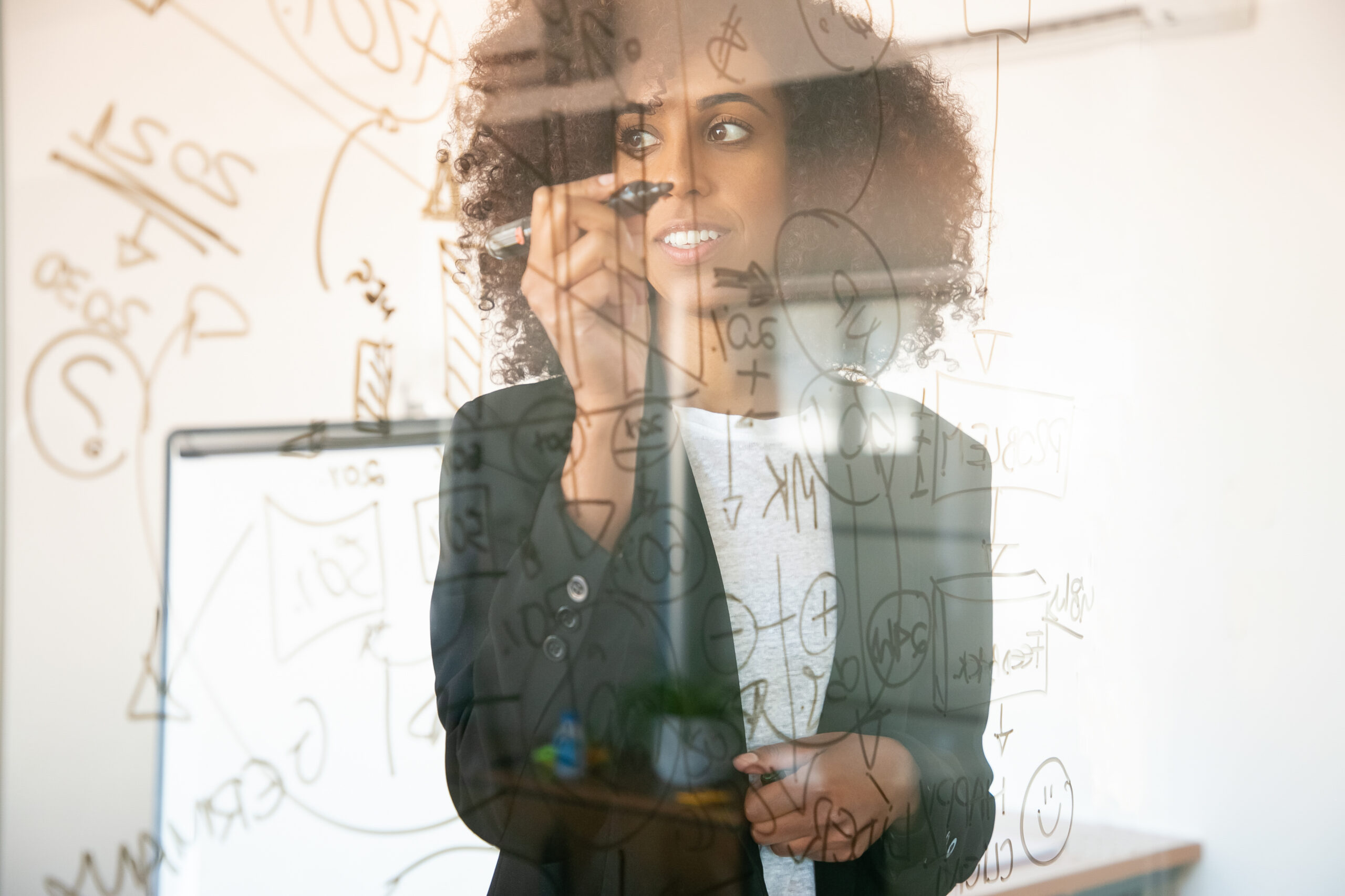 Pretty young businesswomen writing on glass board